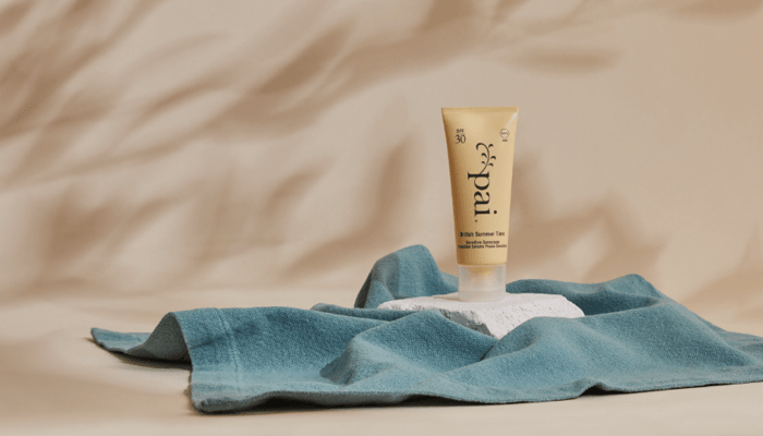 Pai Skincare British Summer Time SPF 30 sunscreen tube on teal linen fabric with warm natural lighting