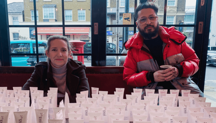 Sarah Brown and team member sitting behind multiple rows of Pai hand sanitiser tubes arranged on table, preparing community giveaway during pandemic