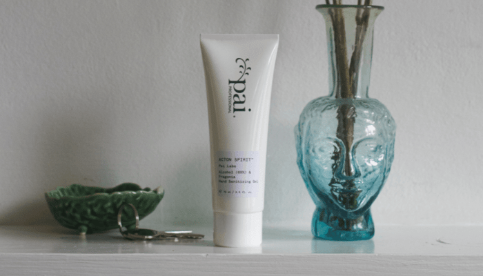 Pai Skincare hand sanitiser tube displayed on white shelf with blue glass vase and green ceramic dish