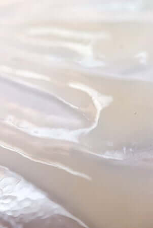 Gentle waves washing onto sandy beach shore, creating a soothing natural pattern reminiscent of smooth eye cream texture