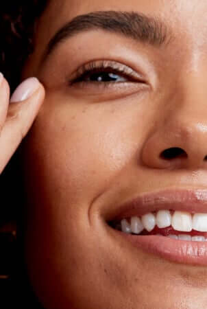 Close-up of woman's smiling face showing healthy eye area with defined brows and glowing skin