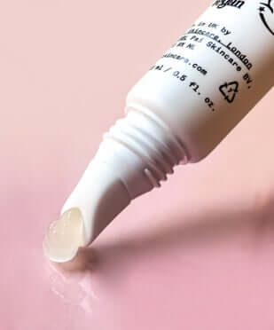 White tube of Pai Echium and Argan Gentle Eye Cream dispensing cream on pink background