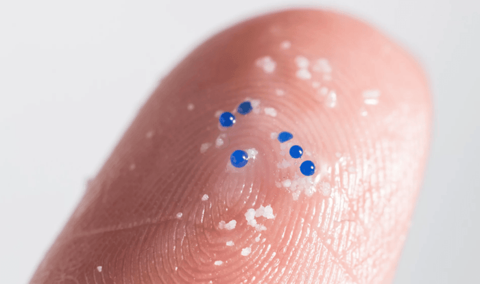 Close-up of fingertip with blue biodegradable jojoba beads from natural exfoliator, showing eco-friendly skincare alternative