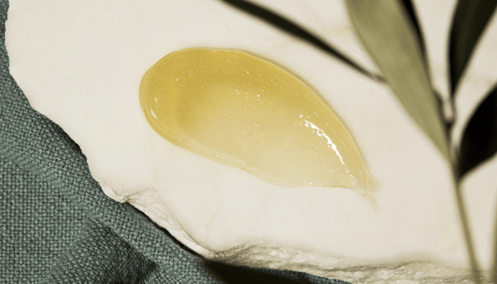 Golden Kukui & Jojoba Bead Exfoliator cream with smooth gel-like texture swatched on white surface with green plant leaves