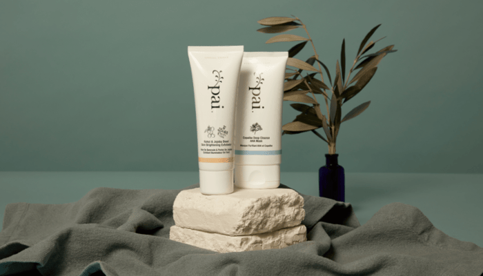 Pai Skincare Kukui & Jojoba Bead Skin Brightening Exfoliator and Copaiba Deep Cleanse AHA Mask on textured stone platform with dried botanicals
