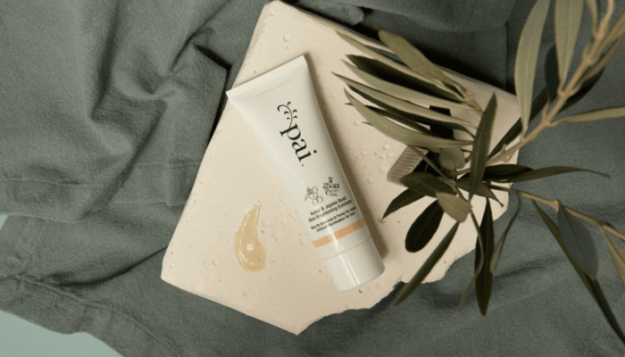Pai Skincare Kukui & Jojoba Bead Skin Brightening Exfoliator tube with product texture on sage green linen