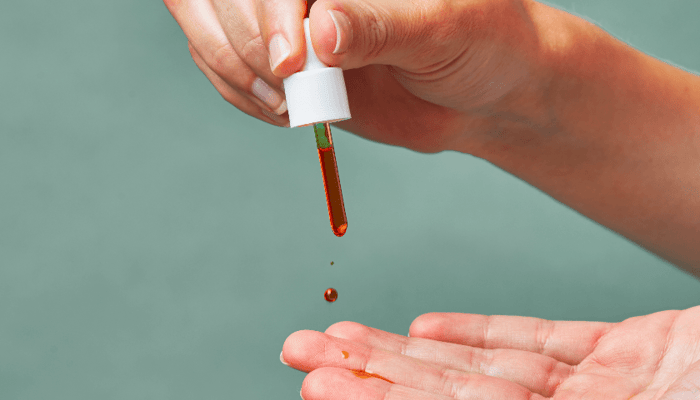 Hands dispensing vibrant orange Pai Rosehip BioRegenerate Oil drops from dropper bottle
