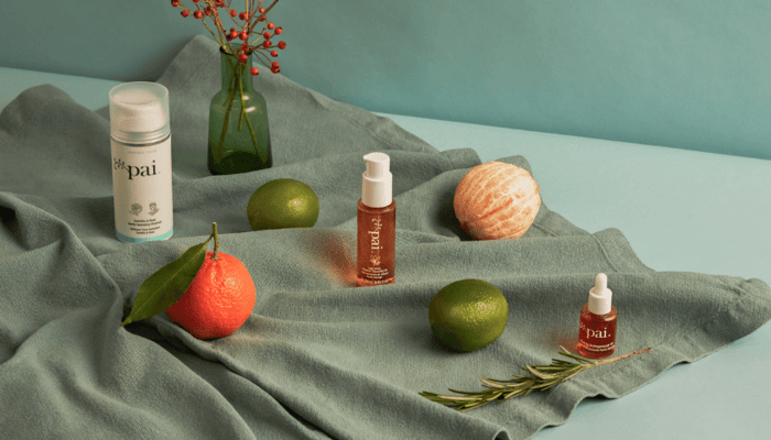 Pai skincare oils artfully arranged with fresh citrus fruits and rosemary on sage green fabric