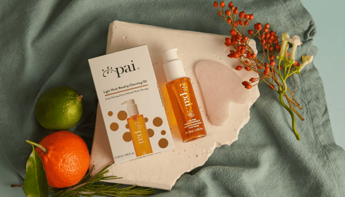 Light Work Rosehip Cleansing Oil bottle and Rose Quartz Gua Sha tool arranged on grey linen with citrus fruits and berries