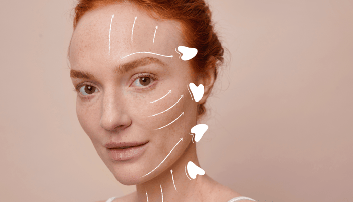 Red-haired woman demonstrating gua sha massage techniques with white directional arrows showing upward and outward facial movements