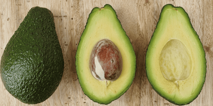 Fresh avocados on wooden surface showing whole fruit and halved pieces with pit, rich in healthy fats for skin health