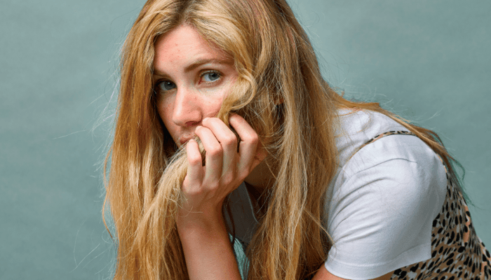 Young blonde woman looking concerned while touching her face, representing skin concerns and acne worries