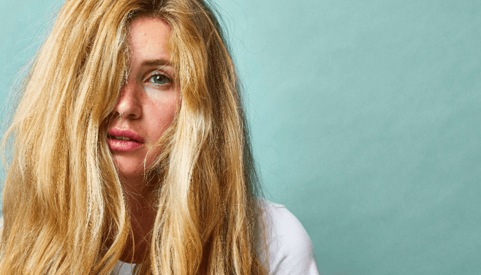 Young woman with blonde hair and natural makeup showing clear healthy skin against mint green background