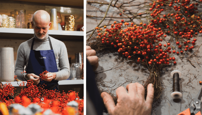 Man in apron crafting Christmas wreath with fresh rosehip stems and bright red berries in rustic kitchen
