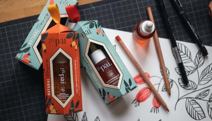 Pai Skincare Natural Treasures Collection gift boxes with botanical illustrations, surrounded by colored pencils and artwork sketches