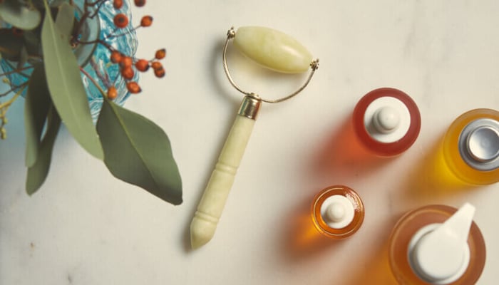 Jade facial roller with natural skincare oils including Rosehip BioRegenerate Oil arranged on neutral background