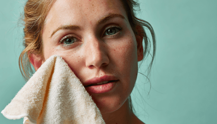 Woman gently pressing soft white exfoliating cloth against her face for sensitive skin cleansing routine