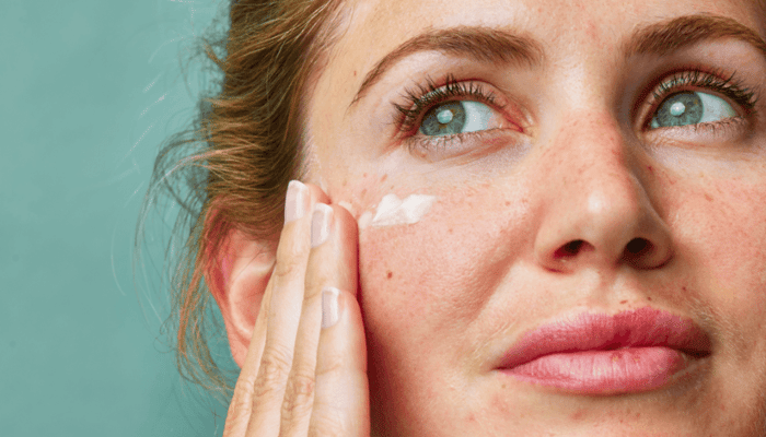Woman applying white facial cream to her cheek, demonstrating moisturizing skincare routine