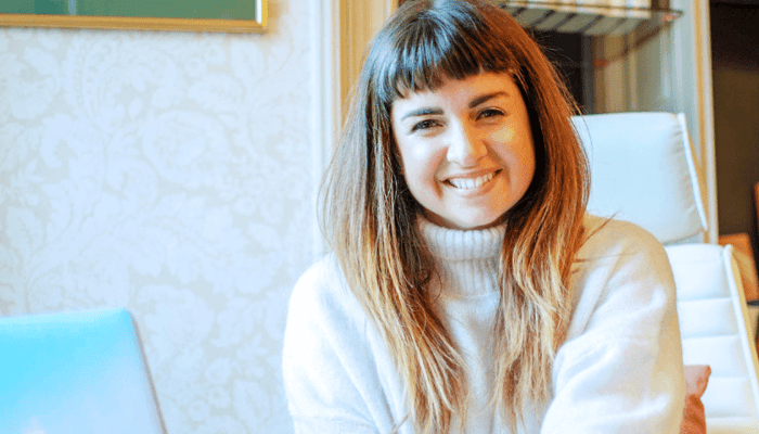 Life coach Lucy Sheridan smiling warmly in cream turtleneck sweater, representing healthy skin wellness