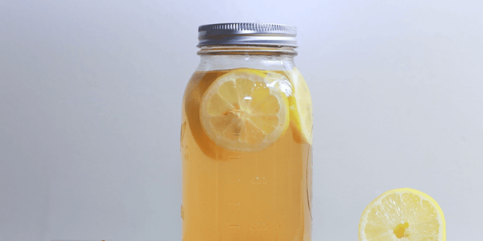 Mason jar filled with lemon-infused water with fresh lemon slices floating inside and lemon wedge beside jar