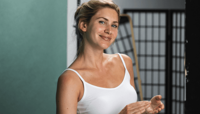 Natural portrait of blonde model Hellana with visible skin texture and rosacea, smiling confidently in white top