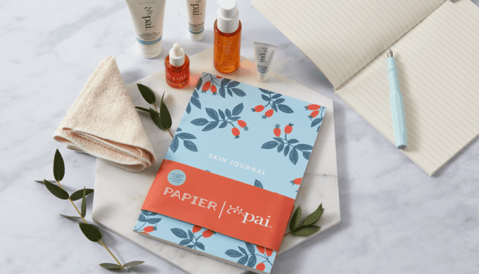 Papier x Pai Skincare collaboration journal with botanical rosehip pattern alongside natural skincare products and towel on marble surface