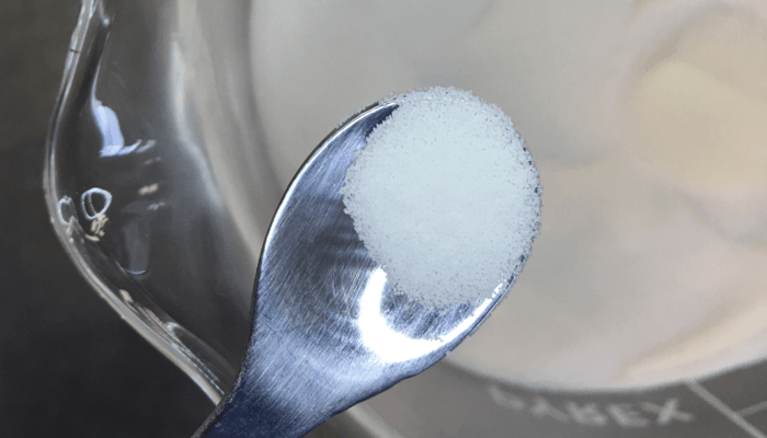 White jojoba wax beads on silver spoon for gentle face exfoliation