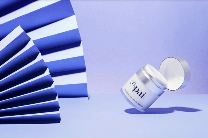 Pai Skincare Light Work Rosehip Cleansing Oil jar with pump dispenser against purple backdrop with blue striped fan