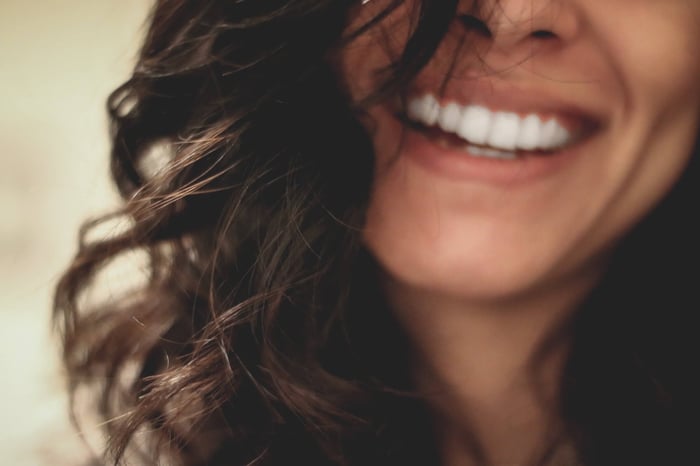 Close-up of woman with curly brown hair smiling, showing healthy glowing skin around eyes