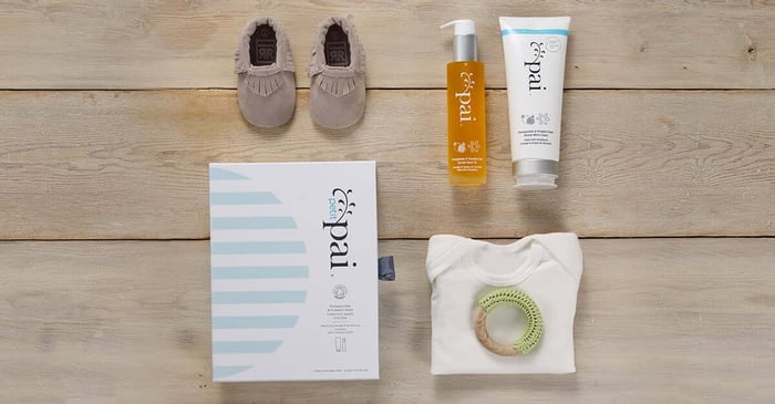 Pai Pregnancy Perfect Stretch Mark System flatlay with baby shoes and teething ring on wooden background