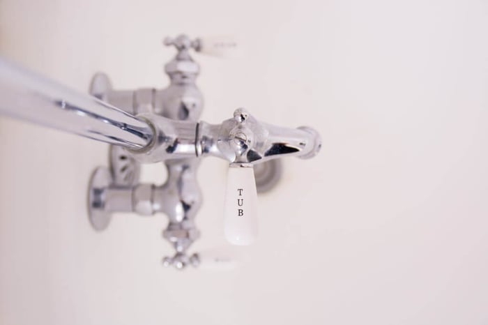 Chrome bathtub taps with white porcelain handles showing TUB marking against clean white bathroom