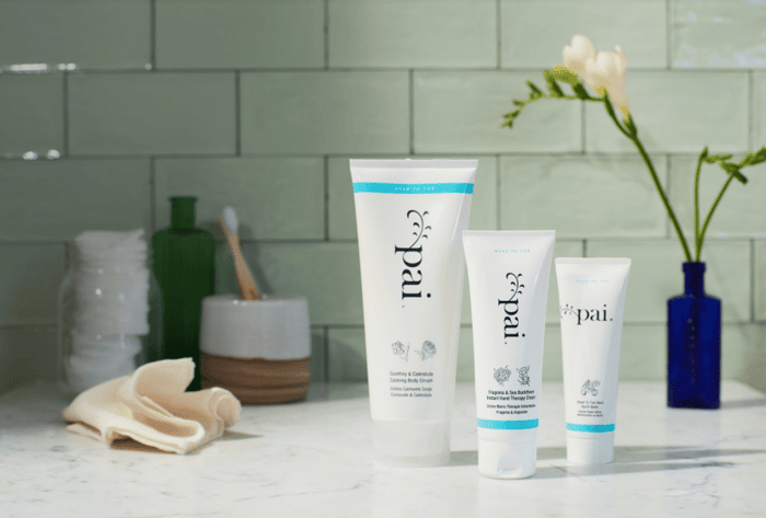 Pai Skincare Comfrey & Calendula Calming Body Cream collection on marble bathroom counter with sage green tiles