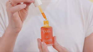 Woman using pipette dropper to apply Pai Rosehip BioRegenerate Oil from orange bottle