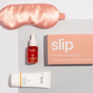 Rose gold silk sleep mask and pink Slip pillowcase with Pai skincare products flatlay on white background