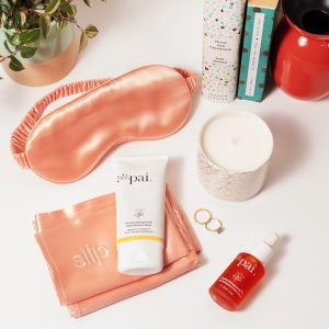 Pink silk eye mask and Pai Skincare moisturiser arranged with beauty accessories on white marble surface