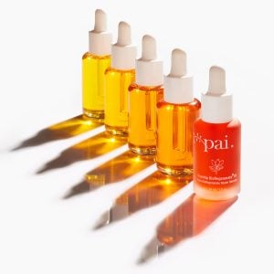 Row of five golden Rosehip BioRegenerate Oil bottles with droppers casting dramatic shadows on white surface