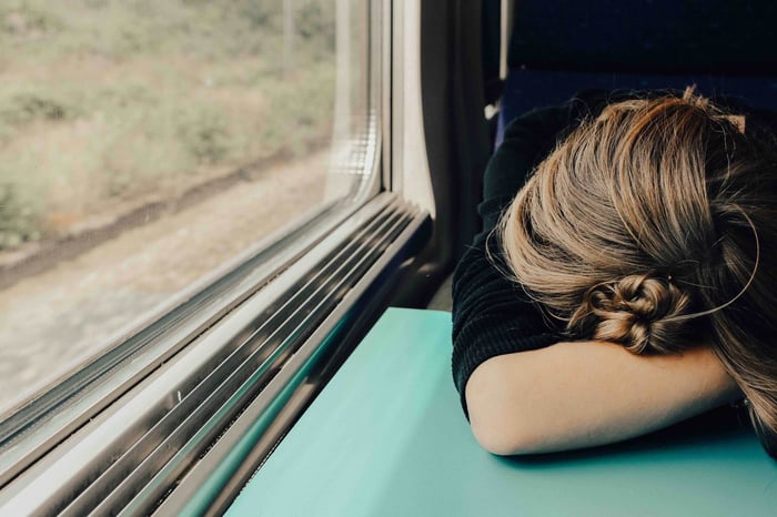 Woman resting her head on arms while looking out train window, representing stress and fatigue as skin triggers