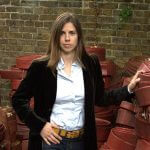 Professional woman in black blazer and white shirt sitting confidently against brick wall backdrop