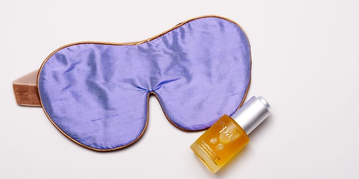 Purple silk sleep mask with brown leather strap alongside Pai Rosehip BioRegenerate Oil for overnight skin repair
