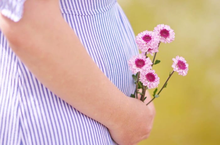 Pregnant woman in blue striped shirt holding pink flowers against yellow background