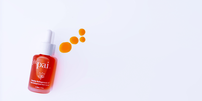 Rosehip BioRegenerate Oil red bottle with orange oil droplets floating above on light purple background