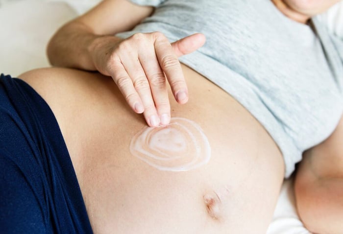 Pregnant woman applying moisturizer cream in circular motions on her belly for pregnancy skincare