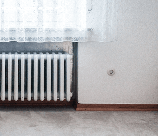 White radiator against wall with lace curtains, showing central heating that can trigger eczema in winter