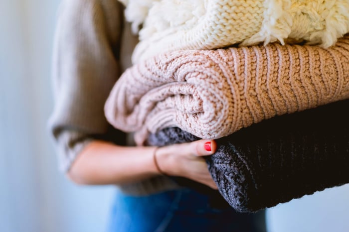 Woman holding stack of cozy knitted wool sweaters in cream and pink colors