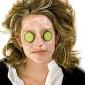 Woman with curly blonde hair wearing cucumber slices over her eyes in classic spa treatment pose