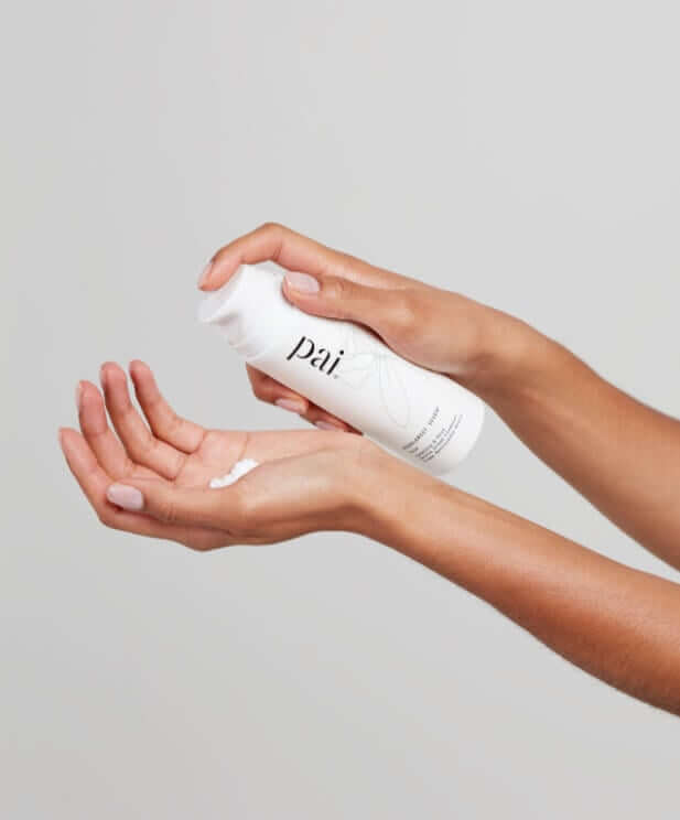 Hands dispensing white cleansing product from Pai Skincare pump bottle into palm for double cleansing routine