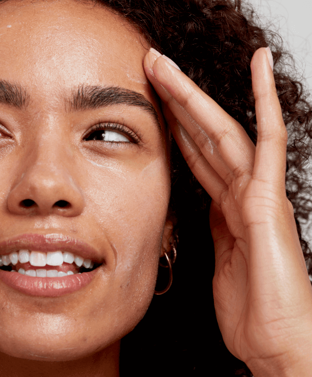 Smiling woman with curly hair touching her glowing, clean face after double cleansing skincare routine