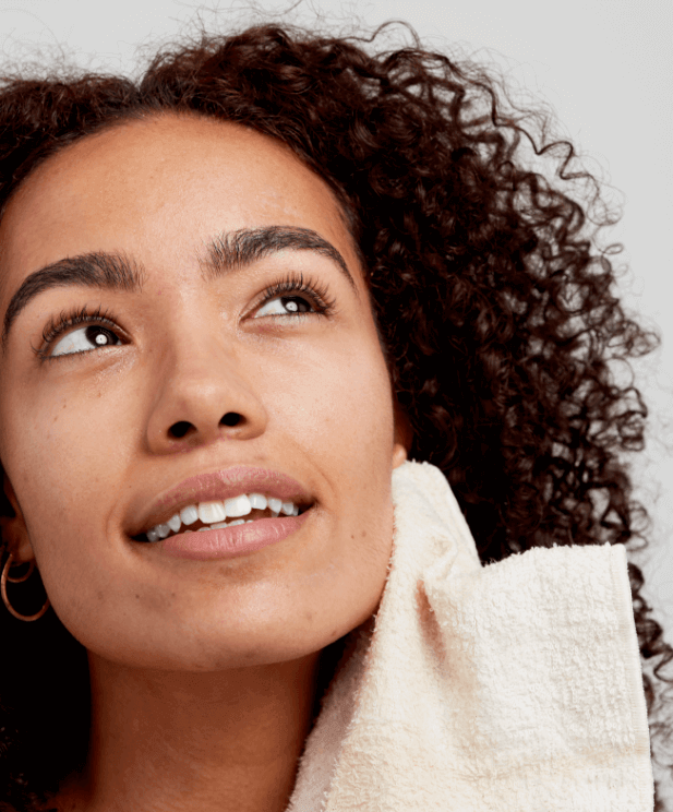 Woman with curly hair holding white cleansing towel, showcasing glowing skin from double cleansing routine