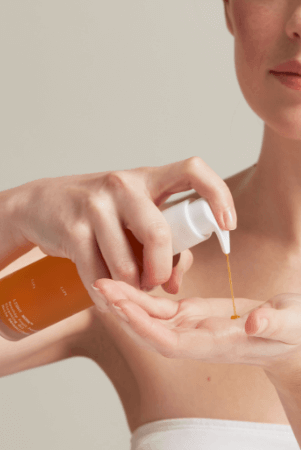 Woman dispensing golden cleansing oil from amber bottle into palm of hand for double cleansing routine