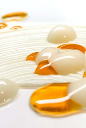 Golden facial oil droplets and clear serum beads on white textured surface for eczema-prone skin care
